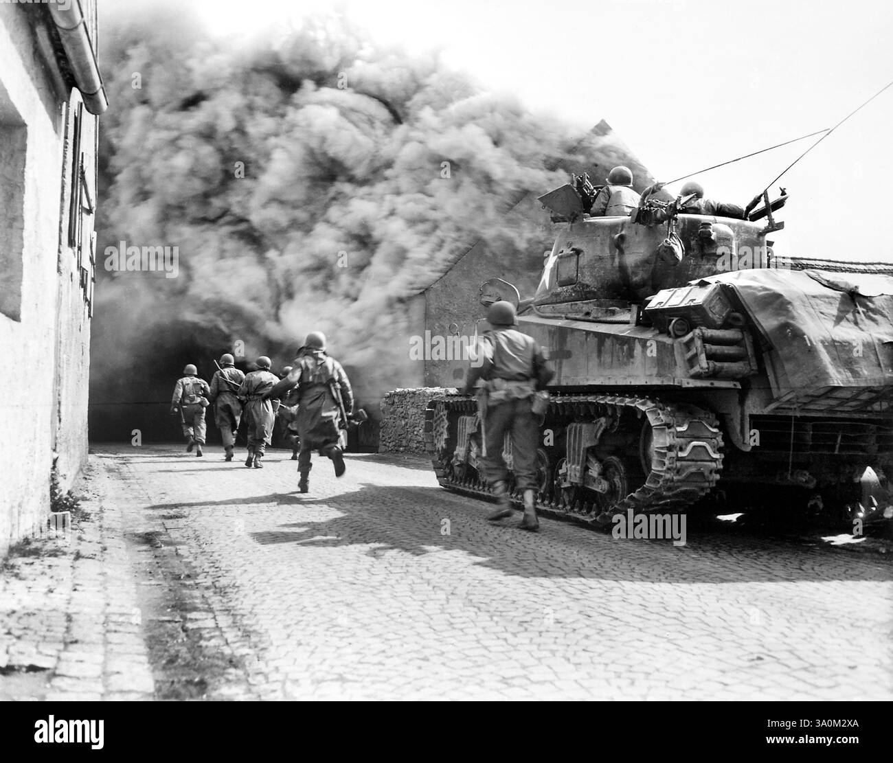Soldats américains du 55th Armored Infantry Battalion et char du 22nd Tank Battalion, se déplaçant dans une rue remplie de fumée, Wernberg, Allemagne, U.S. Army signal corps, 22 avril 1945 Banque D'Images
