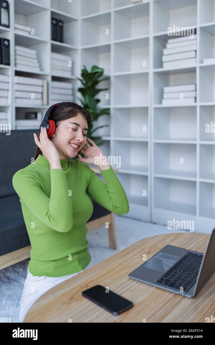 Femme se relaxant sur le canapé porter des écouteurs, écouter de la musique tout en utilisant l'ordinateur dans la maison confortable. Banque D'Images