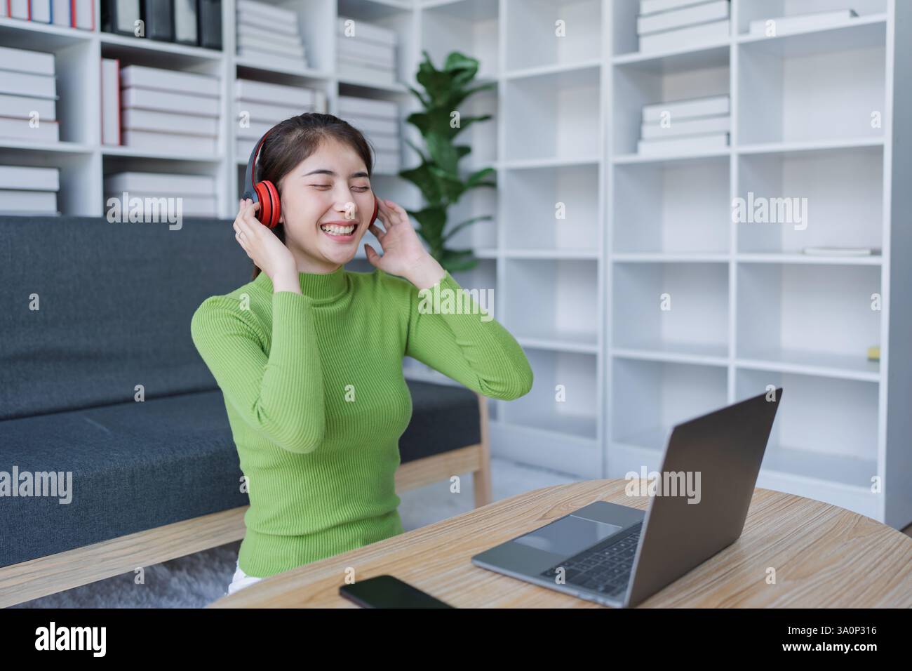 Femme se relaxant sur le canapé porter des écouteurs, écouter de la musique tout en utilisant l'ordinateur dans la maison confortable. Banque D'Images
