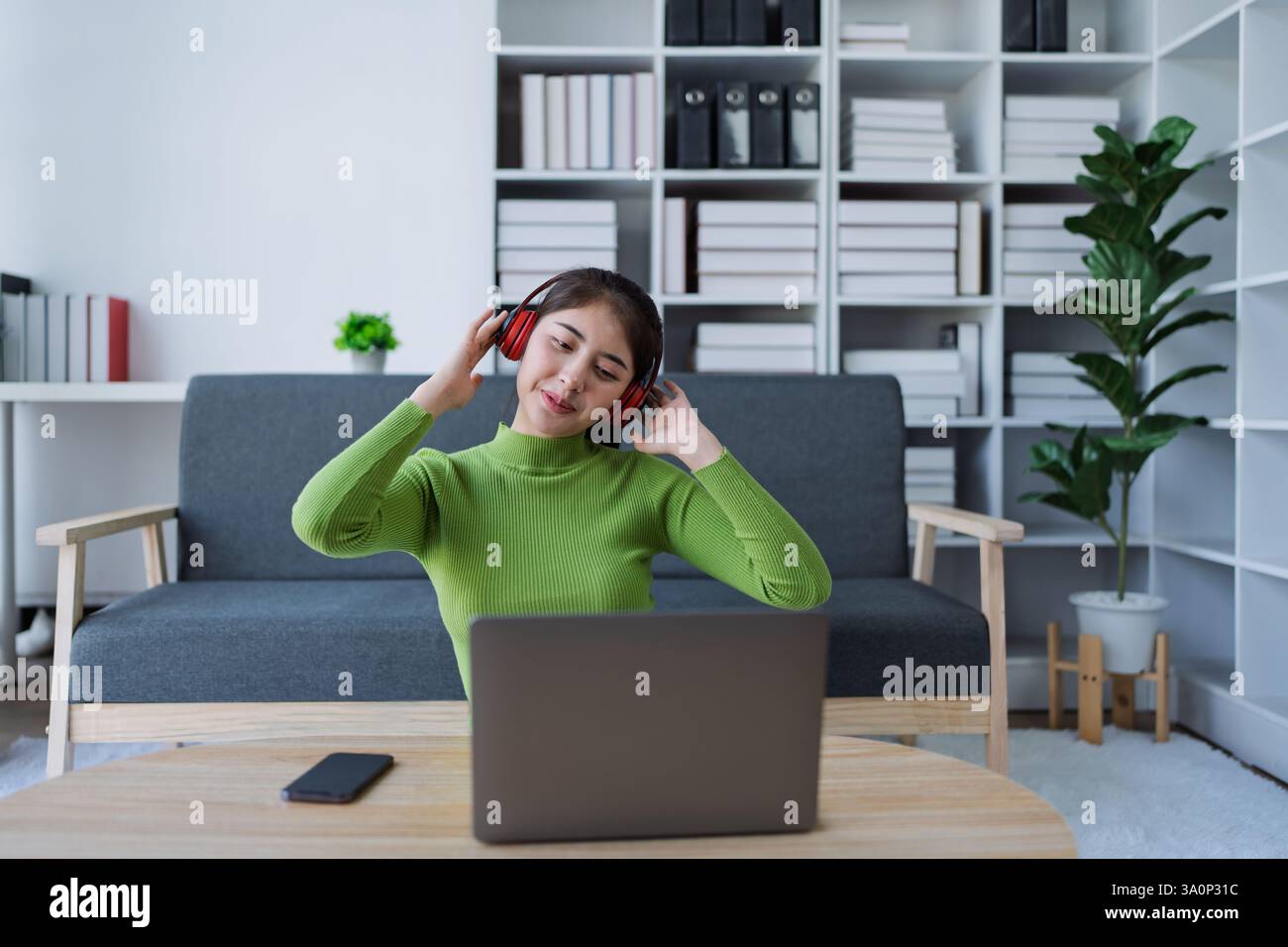 Femme se relaxant sur le canapé porter des écouteurs, écouter de la musique tout en utilisant l'ordinateur dans la maison confortable. Banque D'Images