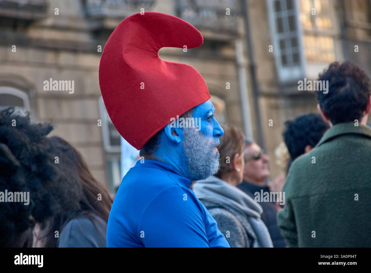 Vigo,Pontevedra,Espagne;4 mars 2025 : Un homme habillé en Schtroumpf se tient parmi la foule au vibrant Carnaval de Vigo en Espagne. Son visage est peint complet Banque D'Images