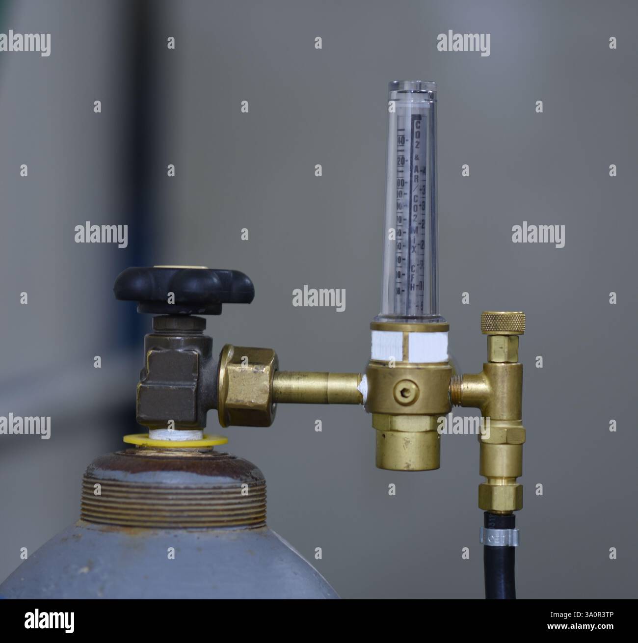 La photo montre une bouteille de gaz avec un régulateur de pression et un débitmètre attaché à elle. Le régulateur de pression est doté d'une poignée noire pour le réglage, une Banque D'Images