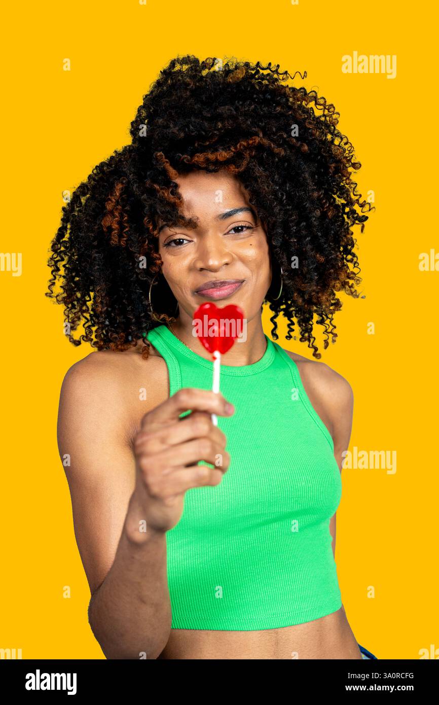 Jeune femme tenant une sucette en forme de coeur sur fond jaune Banque D'Images