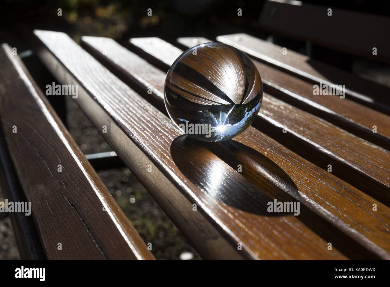 Boule de verre couchée sur un banc avec des lattes en bois, reflétant le soleil, Saxe, Allemagne, Europe Banque D'Images