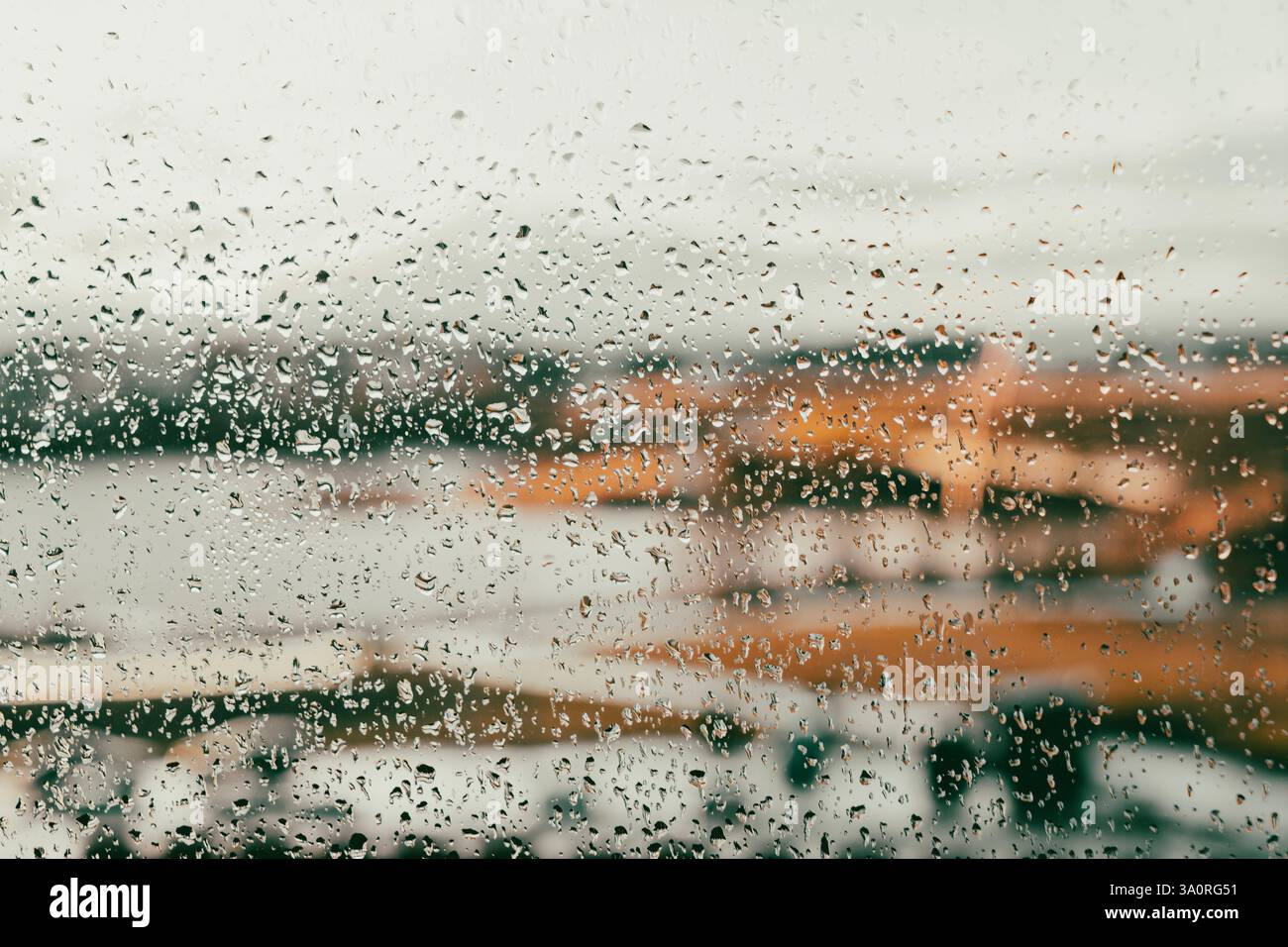 Gros plan de gouttes de pluie sur une fenêtre en verre avec une vue floue d'un paysage dans des tons automnaux chauds. Les gouttelettes créent une atmosphère mélancolique rêveuse Banque D'Images