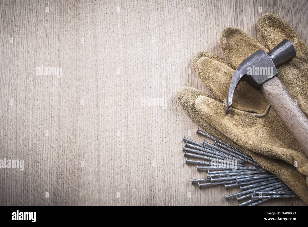 Composition de gants de protection en cuir de marteau à griffes et de longs clous en acier sur le concept de construction de fond en bois Banque D'Images