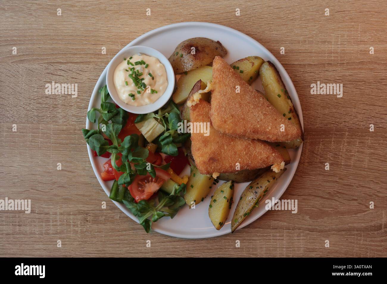 plat principal sur une assiette blanche fromage frit, pommes de terre cuites au four, salade de légumes avec tomates et sauce tartare Banque D'Images