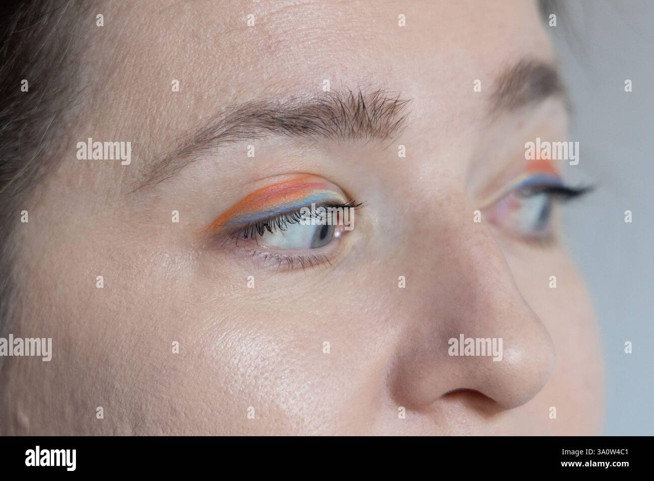 Gros plan détaillé d'un oeil féminin avec eyeliner artistique orange et bleu, mettant en valeur la créativité et l'expression de soi dans le maquillage. Banque D'Images