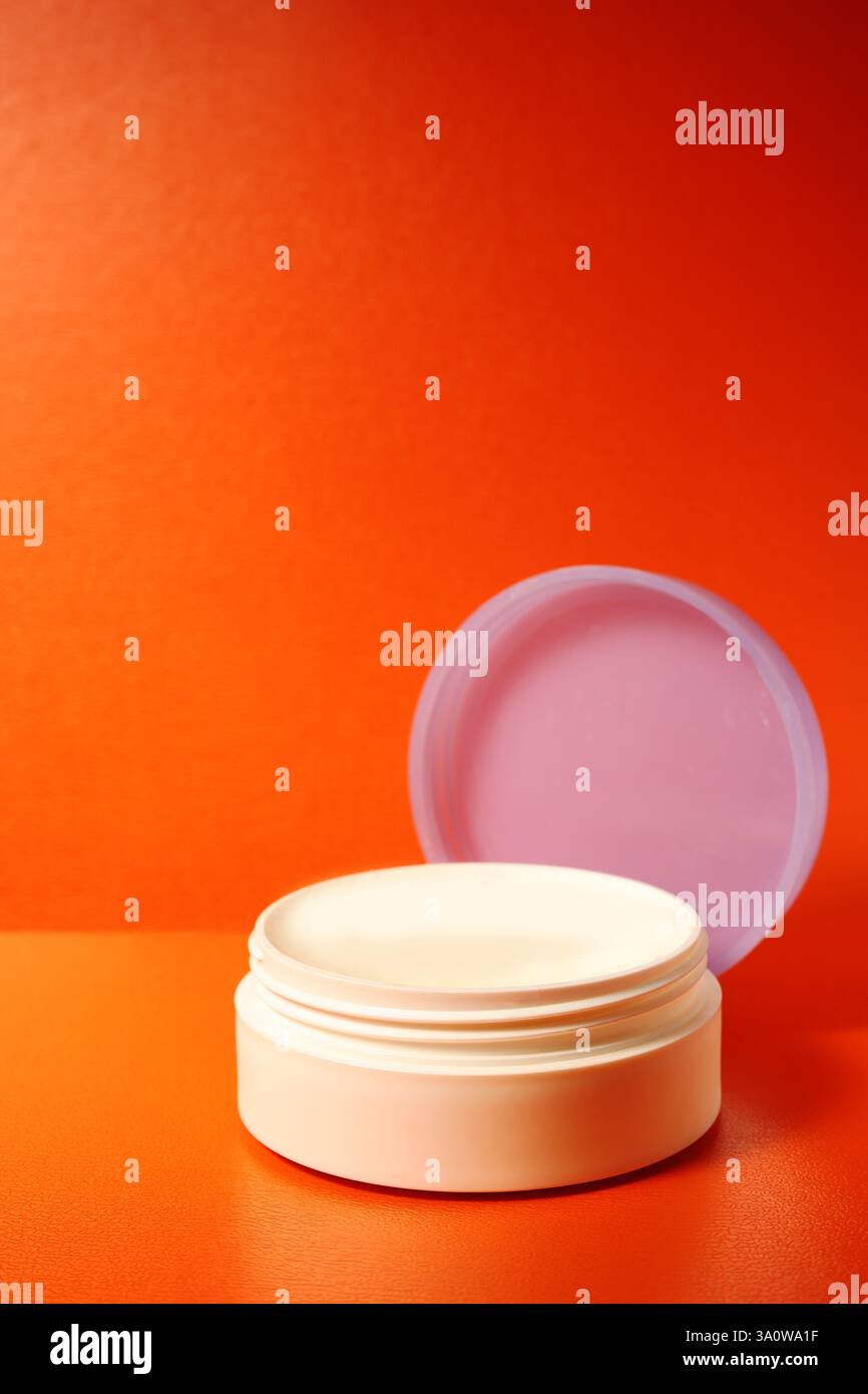 pot de crème visage avec couvercle ouvert sur fond orange. pot vide. Banque D'Images