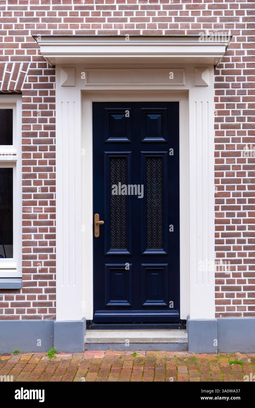 Façade en brique avec élégante porte en bois bleu foncé et cadre blanc classique Banque D'Images