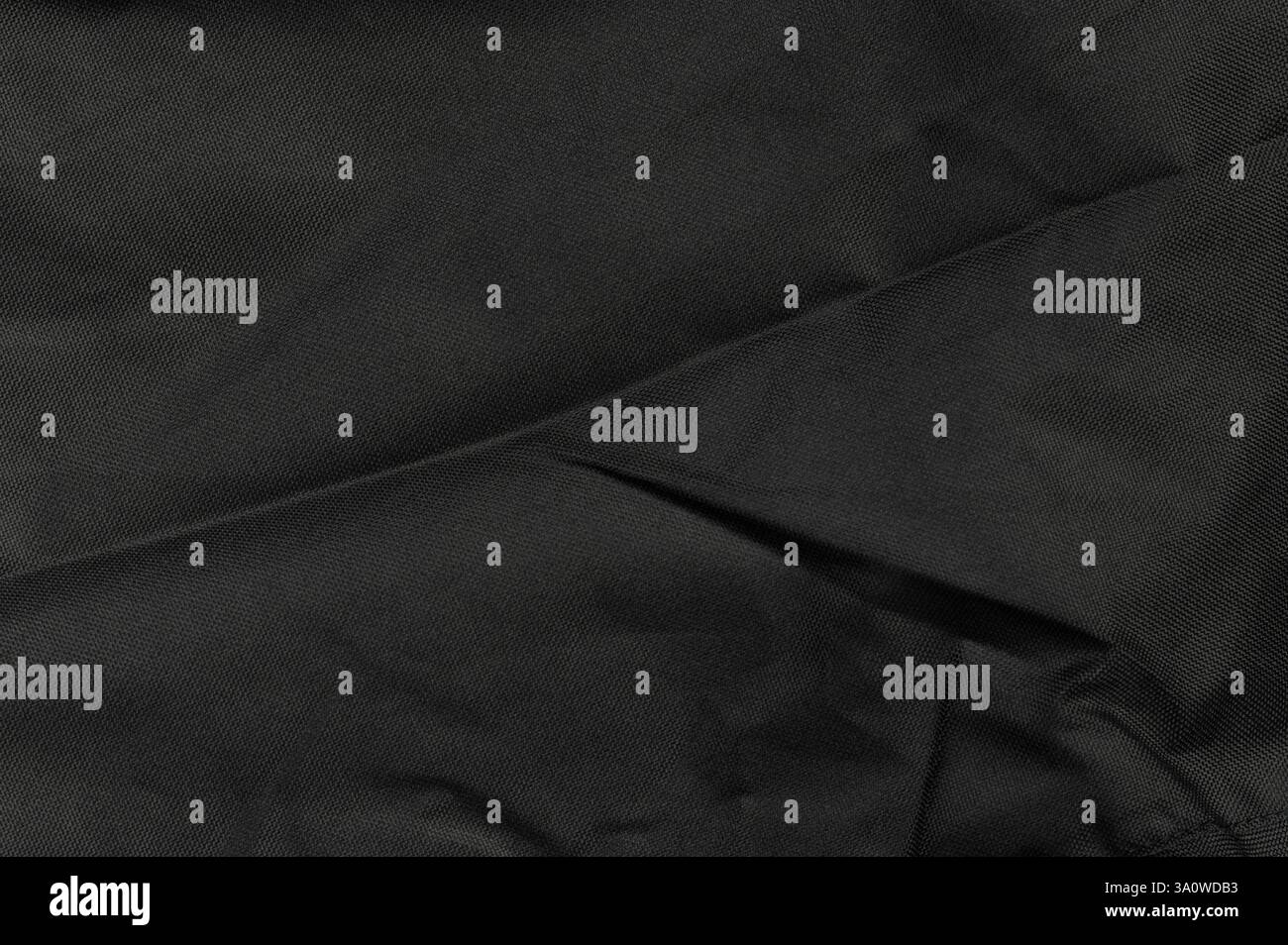 Le tissu noir texturé montre des détails complexes avec des plis doux et des ombres sous un éclairage doux dans un cadre confortable. Banque D'Images