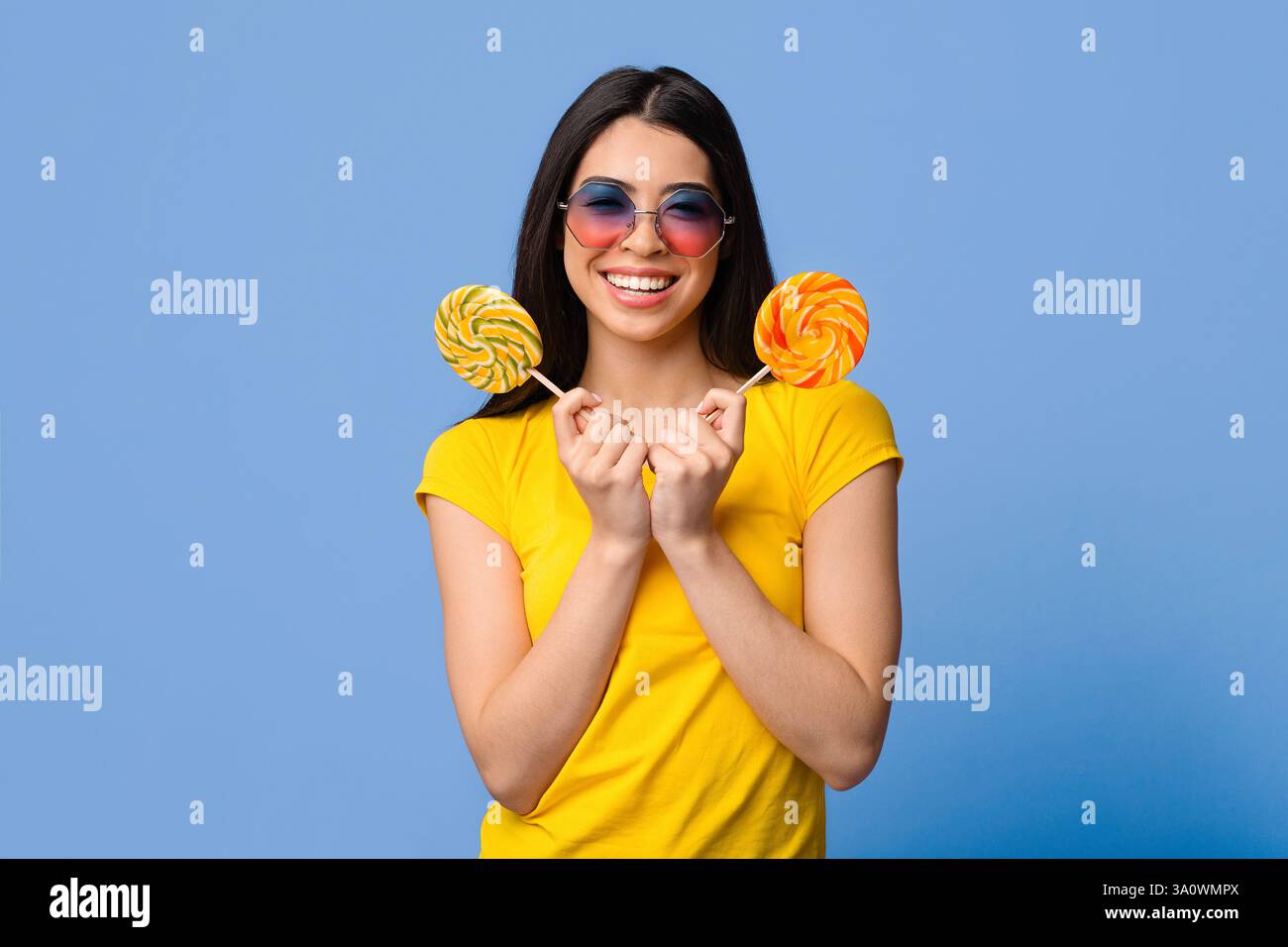 Douceur. Jolie jeune femme d'été couvrant l'oeil avec grand lulllipop lumineux et regardant la caméra, fond jaune avec espace de copie Banque D'Images