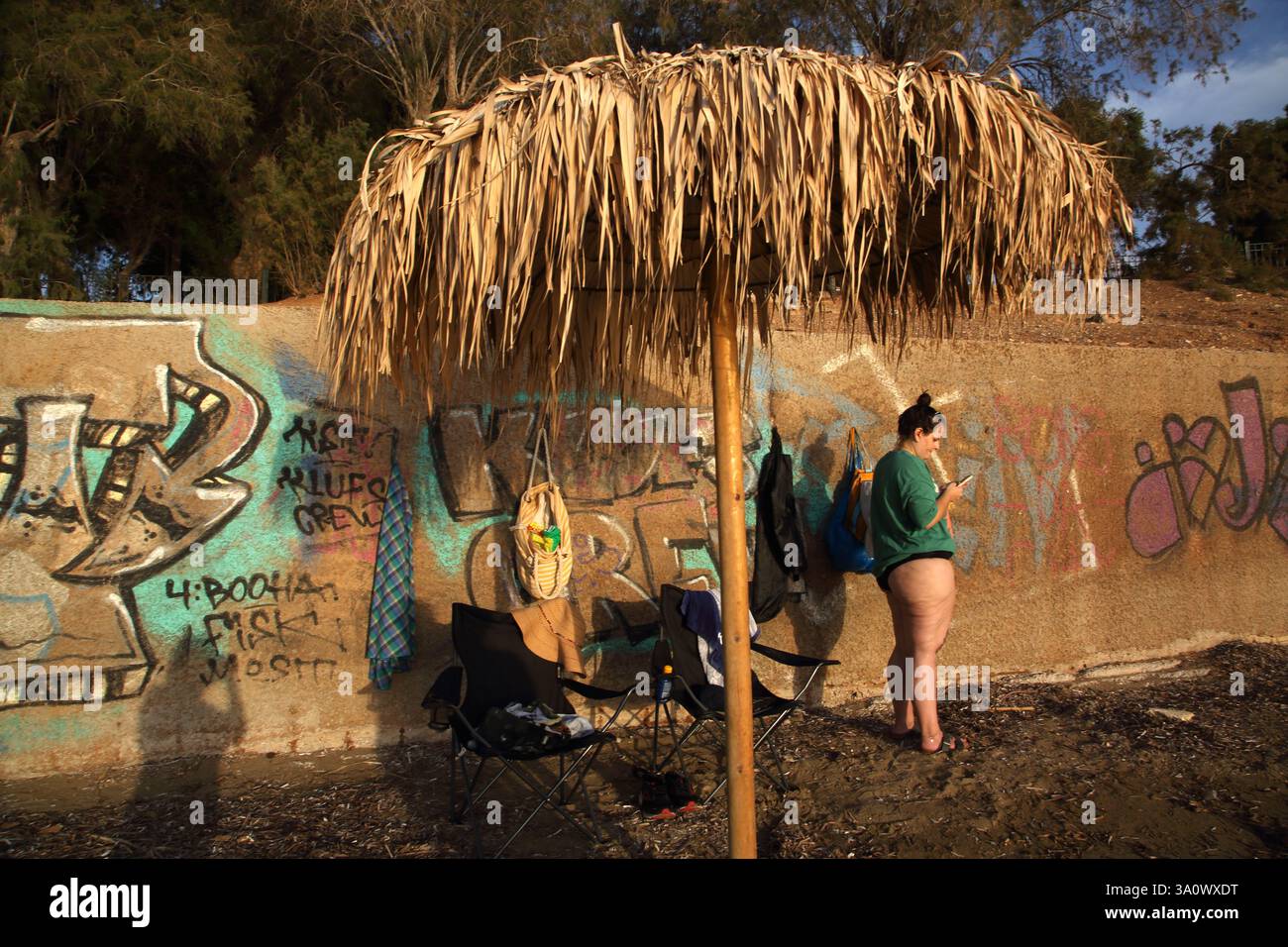Femme utilisant le téléphone portable debout par le mur avec Graffiti à Vouliagmeni Beach Attica Grèce Banque D'Images
