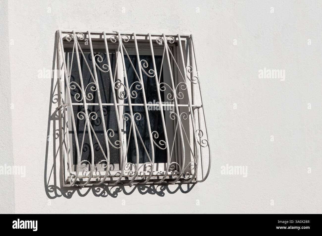Façade blanche avec fenêtre et garde-corps en fer forgé. Vue avant de la fenêtre confortable avec gardes et barres de sécurité sur le mur de la maison. Grille de forge décorative dans un w Banque D'Images