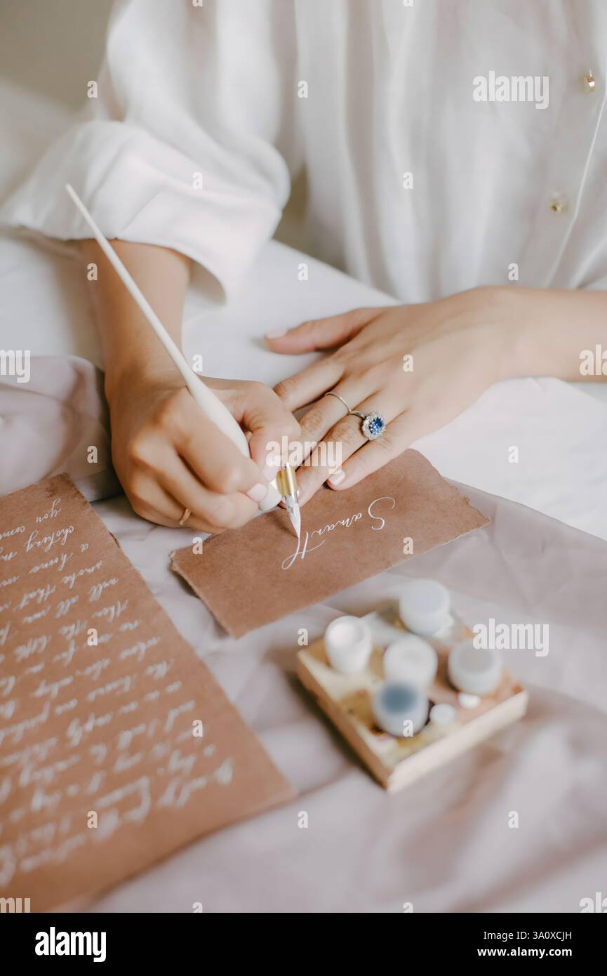 Les mains pratiquent habilement la calligraphie sur papier texturé tout en étant entourées de pots d'encre colorés dans un cadre serein. Banque D'Images