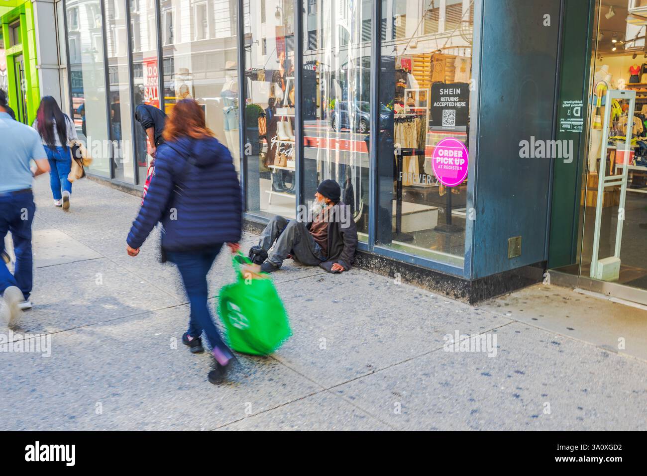 Mendiant sans abri assis sur le trottoir près de l'entrée du magasin tandis que les piétons passent sur la 34e rue à New York. New York. ÉTATS-UNIS. Banque D'Images