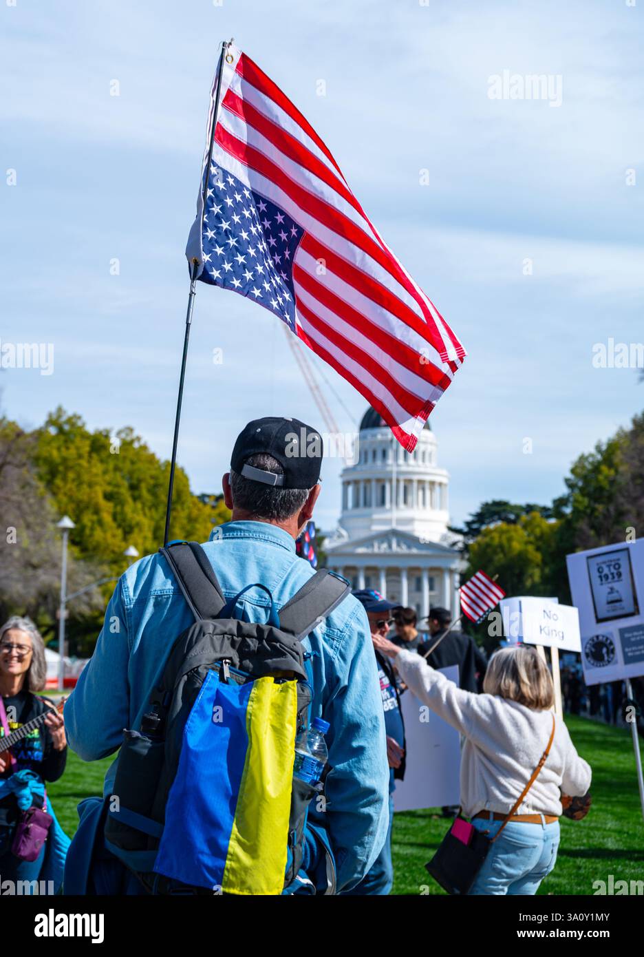 Sacramento, CA États-Unis - 4 mars 2025 : un homme avec un sac à dos de couleur ukrainienne porte un drapeau américain renversé marchant lors de la Démorac du 4 mars 50501 Banque D'Images