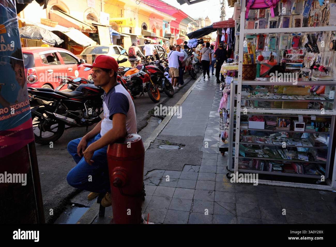 Un vendeur masculin qui vend des étuis de téléphone portable assis près d'une bouche d'incendie sur le trottoir avec sa stalle en arrière-plan dans Mercado Municipal.Granada.Nicaragua Banque D'Images