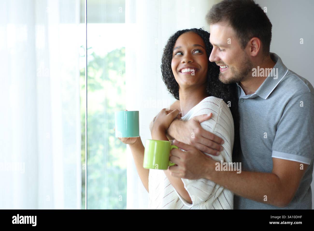 Heureux couple interracial buvant et se regardant à la maison Banque D'Images