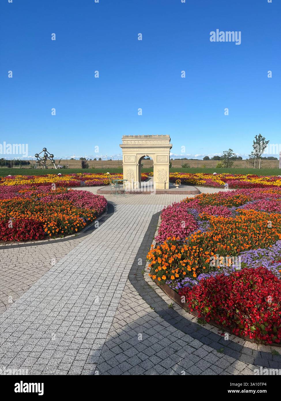 Une plus petite réplique de l'Arc de Triomphe, magnifiquement placé dans un jardin luxuriant entouré de fleurs vibrantes et colorées. - Image de stock capturée avec un smartphone