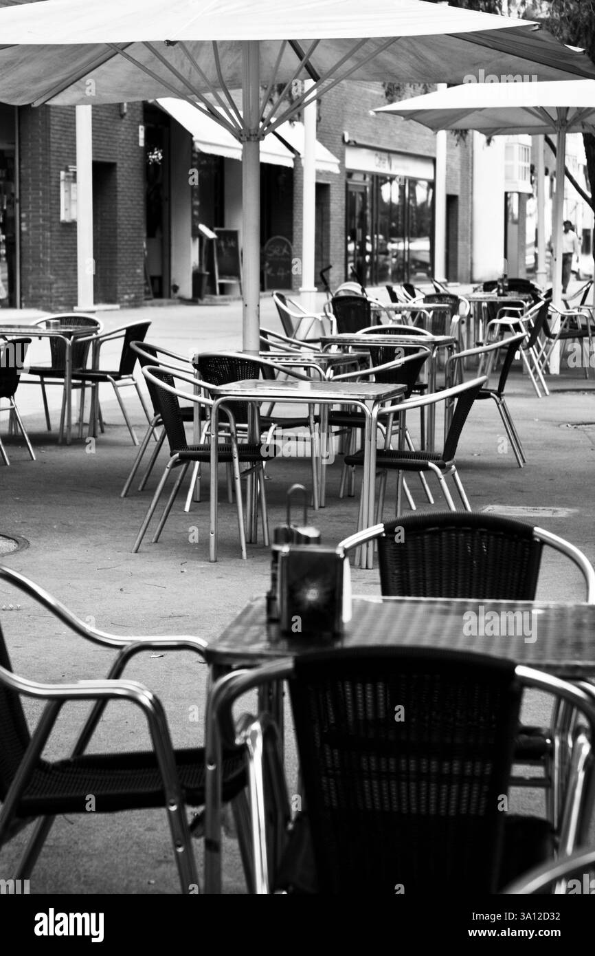 Tables en métal modernes et chaises tissées dans un café extérieur vide. Noir et blanc, design minimaliste et toile de fond architecturale. Banque D'Images