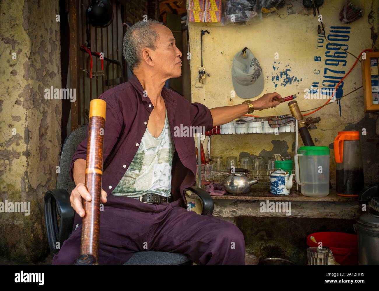 Un vendeur de rue vendant du thé vert cherche un briquet pour fumer du tabac fort à travers sa pipe à eau traditionnelle en bambou. Banque D'Images
