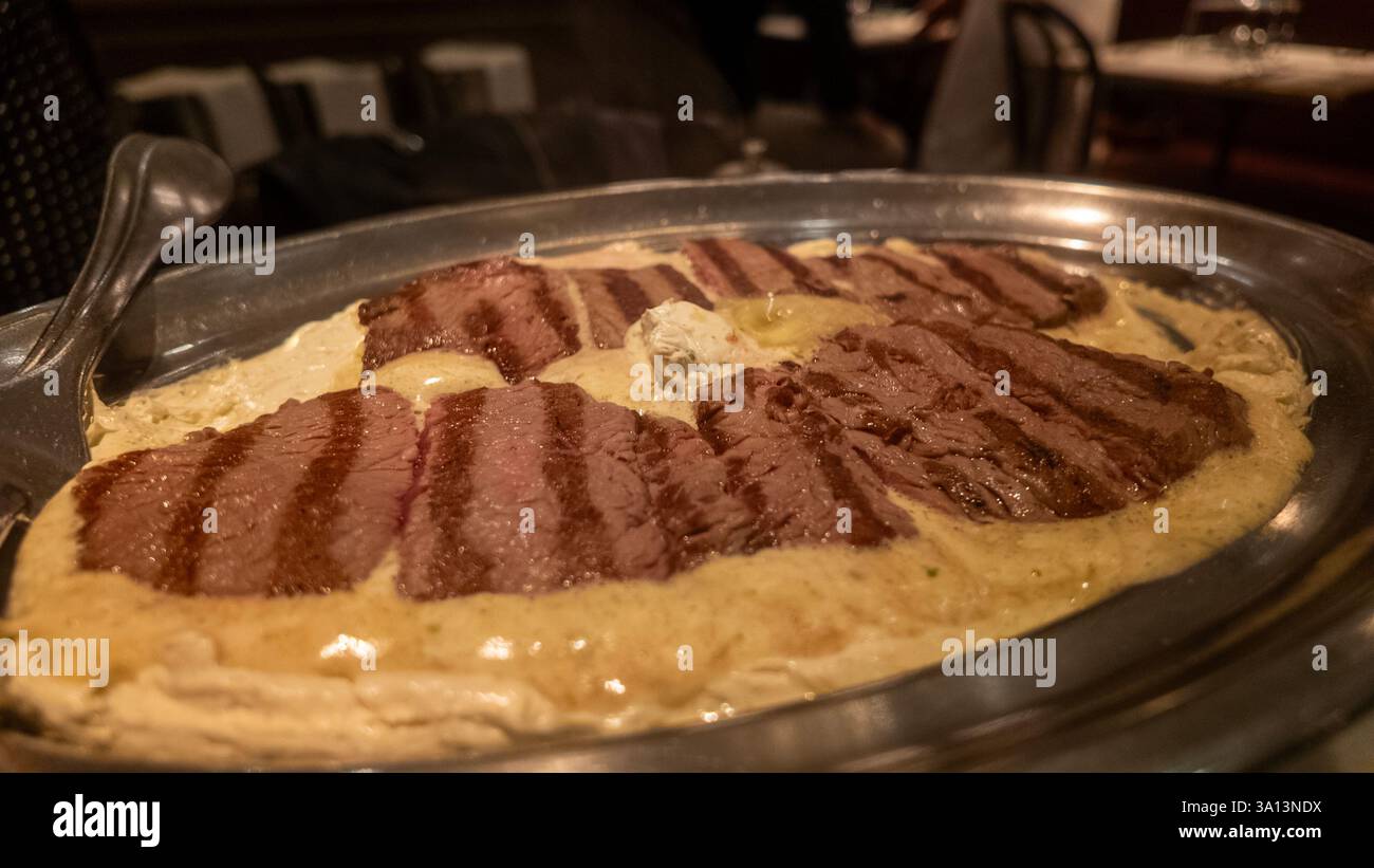 Tranches de filet de bœuf grillé reposant sur un lit de sauce crémeuse et garnies de beurre, servies sur un élégant plateau argenté dans un cadre de restaurant Banque D'Images