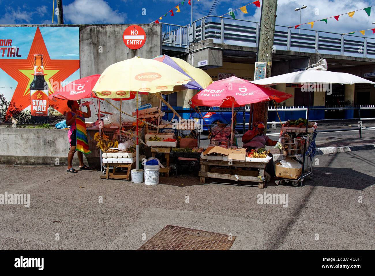 Grenade - Caraïbes - un vendeur de rue vendant une grande variété d'aliments sous des parapluies colorés. Banque D'Images