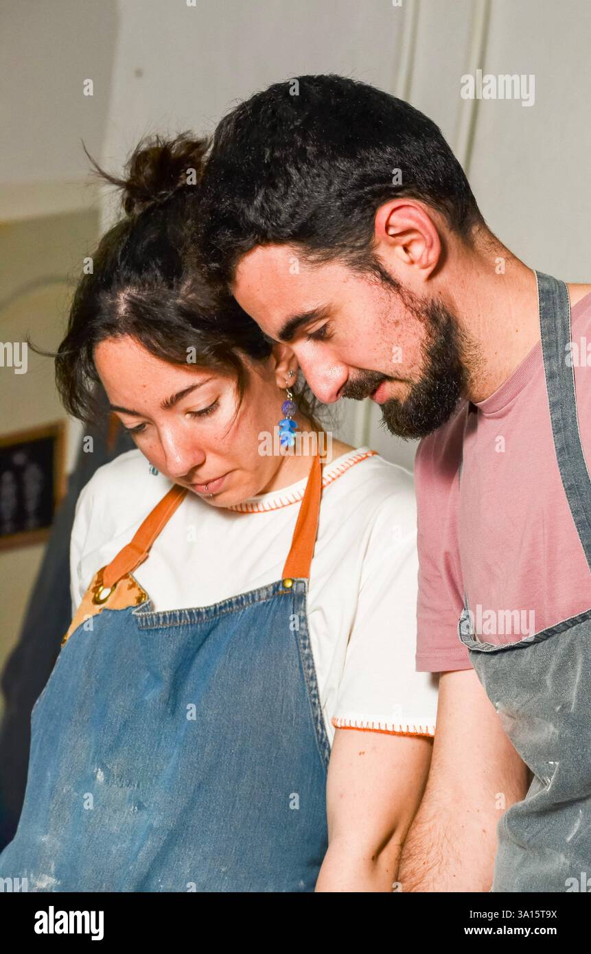 Deux artisans portant des tabliers travaillent ensemble, concentrant leur attention sur un projet de poterie dans leur atelier de céramique Banque D'Images