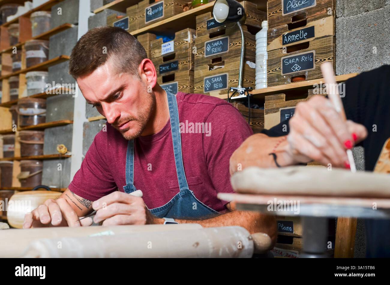 Deux artisans se concentrant sur le façonnage de l’argile dans un atelier de poterie, entourés d’outils et de matériaux Banque D'Images