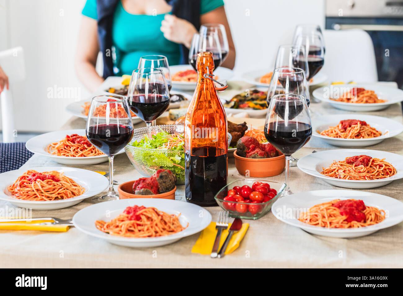 Table pour le déjeuner avec spaghetti à la sauce tomate, boulettes de viande, légumes, tomates cerises et vin rouge Banque D'Images