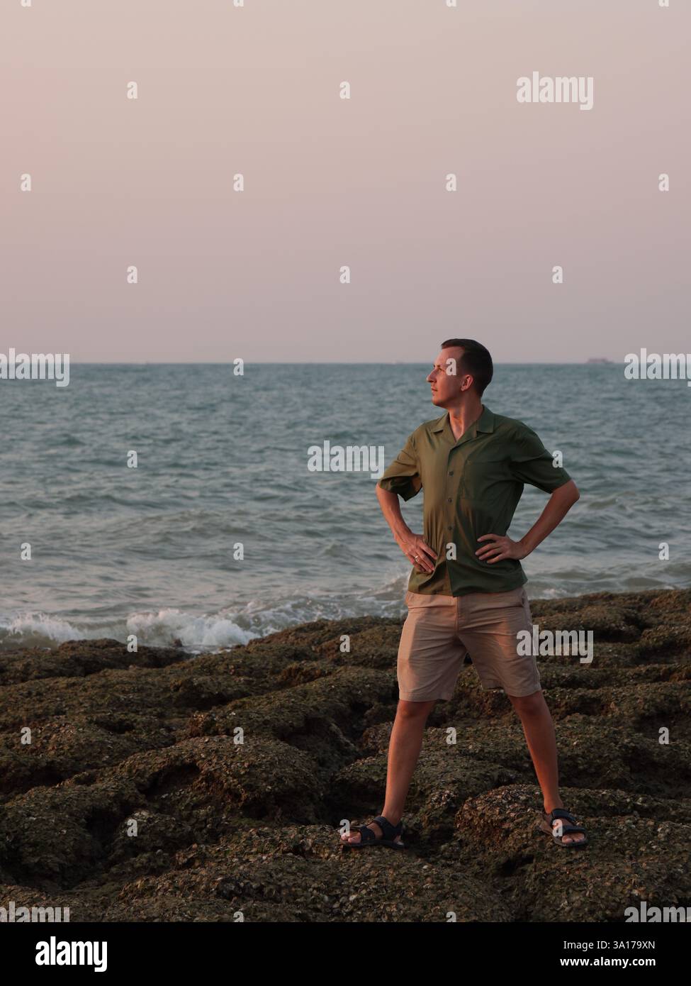 Homme posant avec confiance sur la plage rocheuse pendant le coucher du soleil dans la zone côtière Banque D'Images