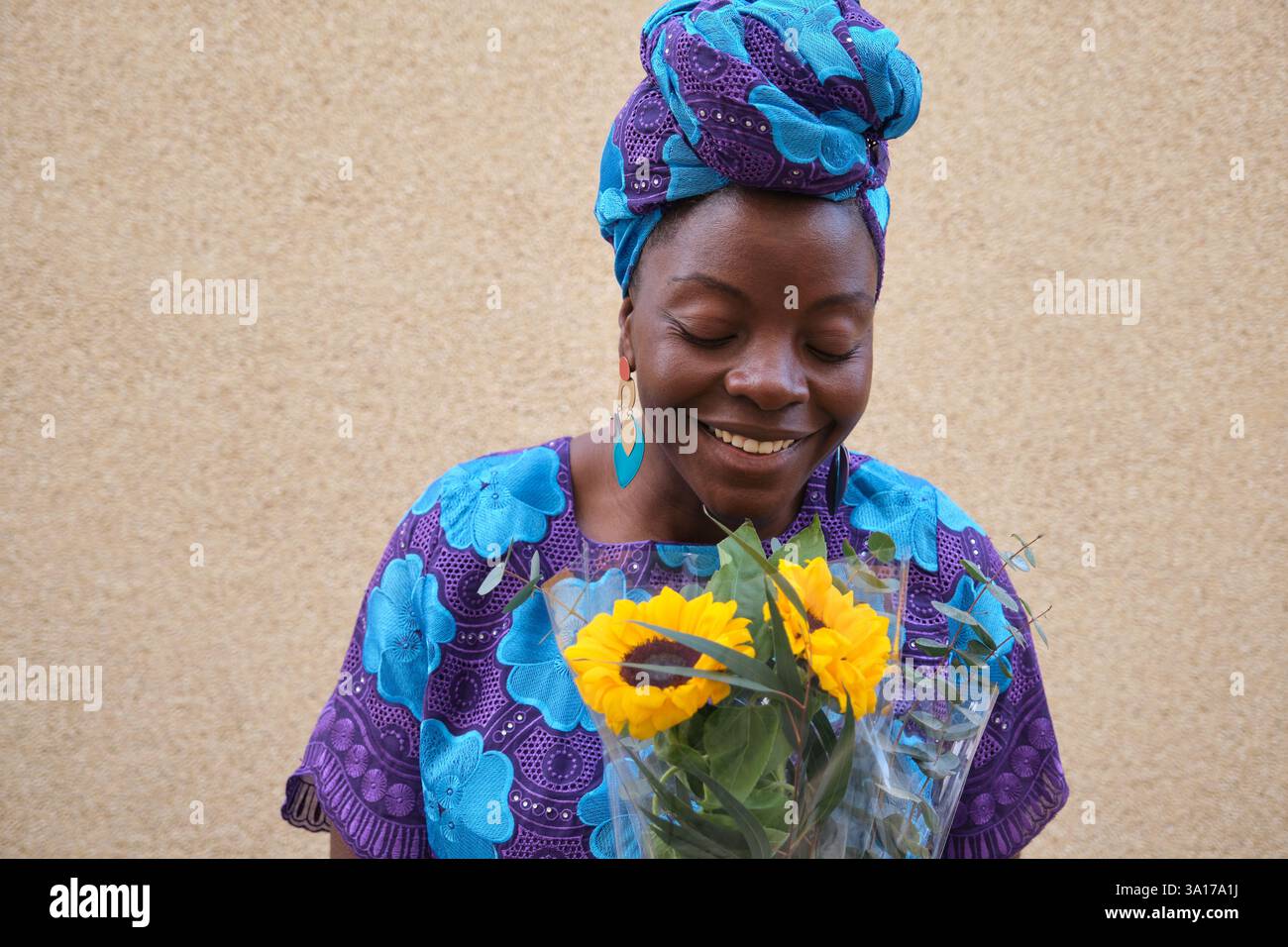 Femme africaine sentant bouquet de tournesols portant des vêtements traditionnels Banque D'Images