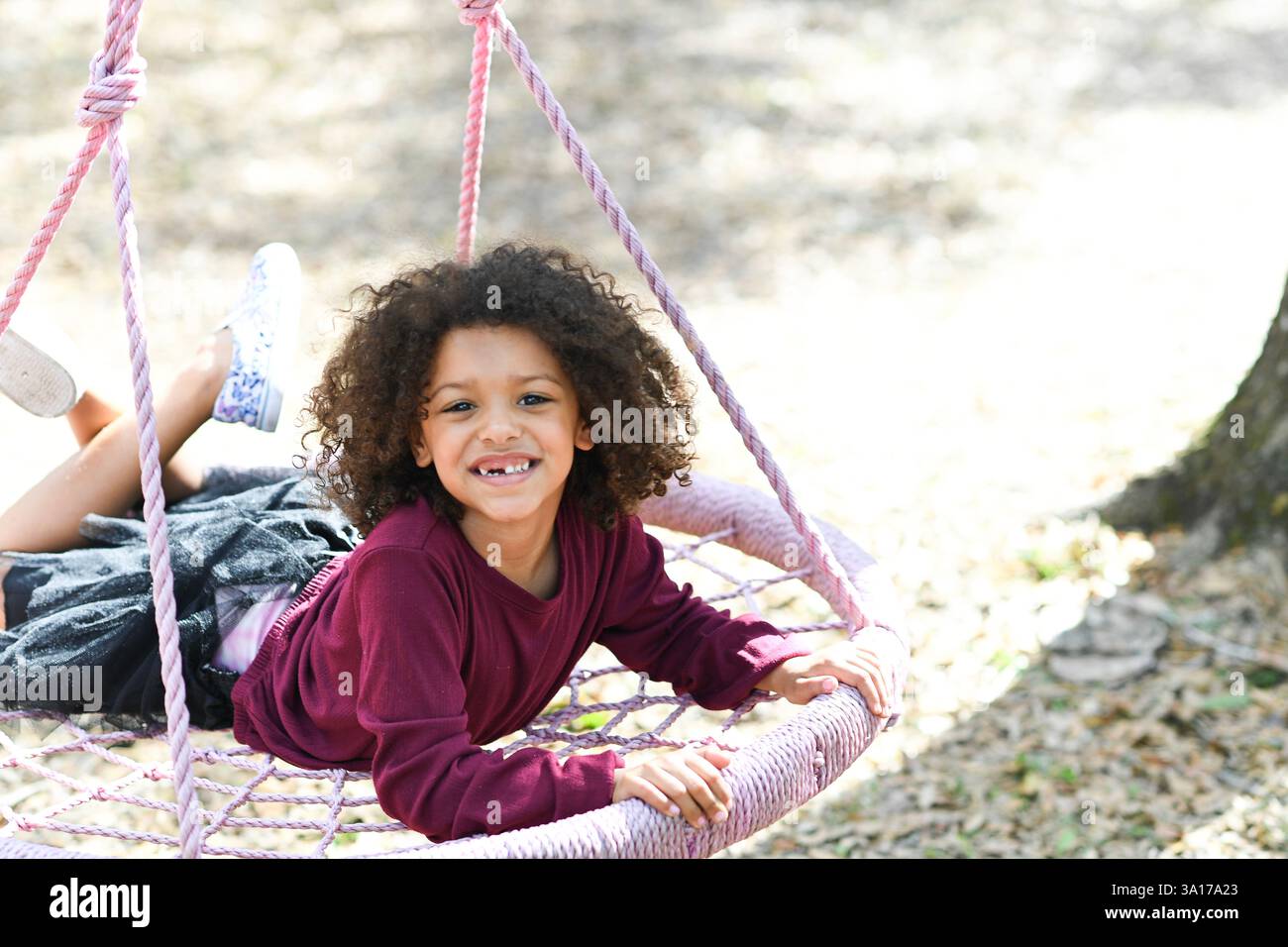 Fille souriante couchée sur une balançoire de corde rose, appréciant playti en plein air Banque D'Images