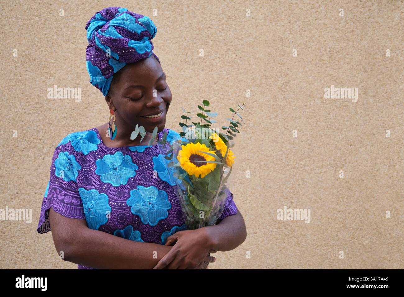 Femme portant une robe africaine traditionnelle tenant des tournesols et souriant Banque D'Images