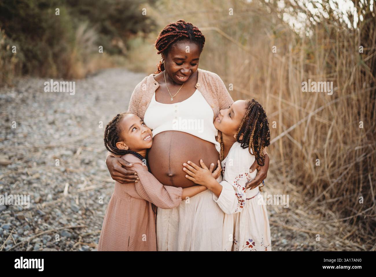 Joyeuses filles de course de mélange souriant embrassant le ventre de maman enceinte noir Banque D'Images