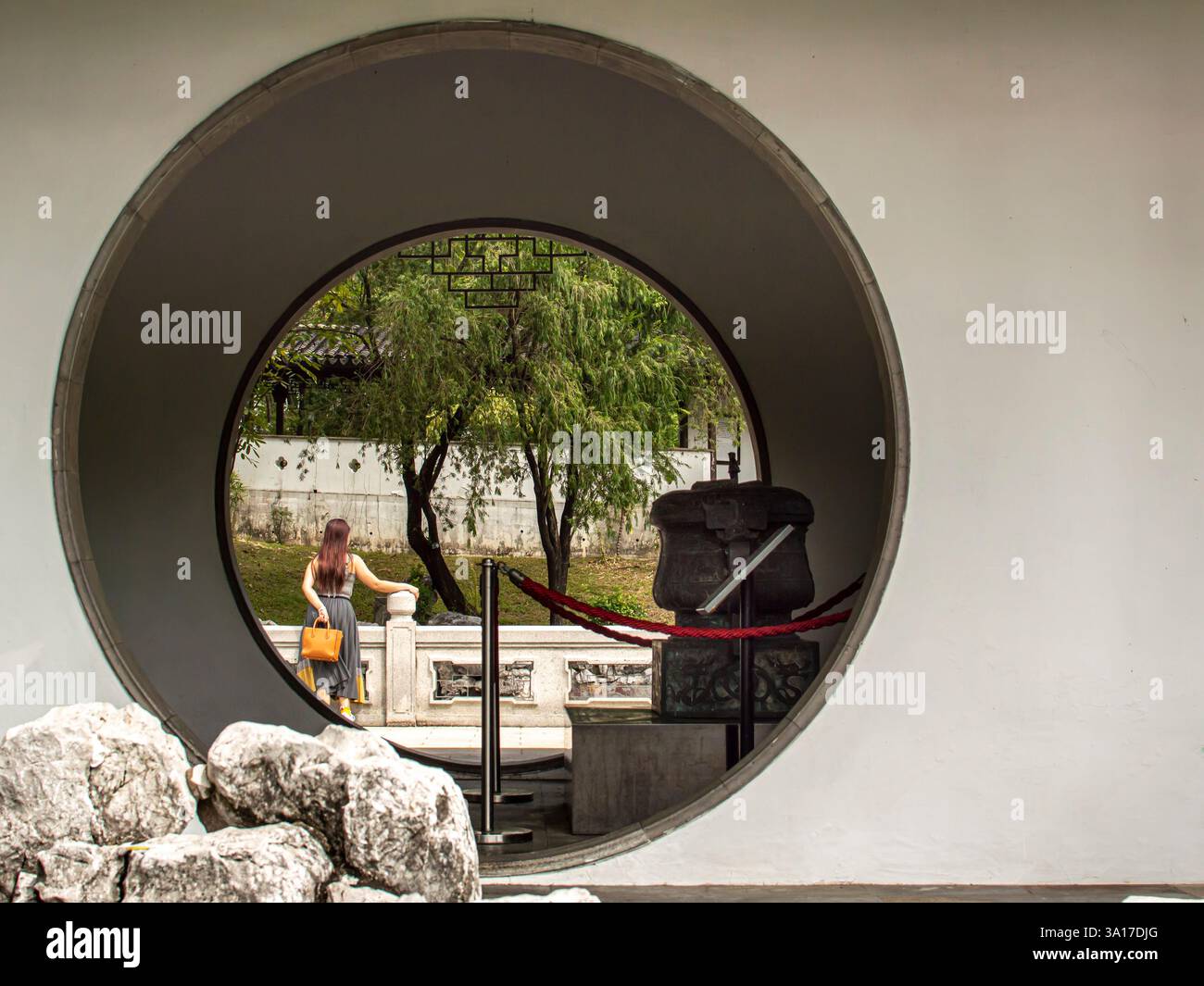 Une scène sereine encadrée par une porte de lune traditionnelle dans un jardin asiatique. Une femme admire les environs paisibles. Banque D'Images