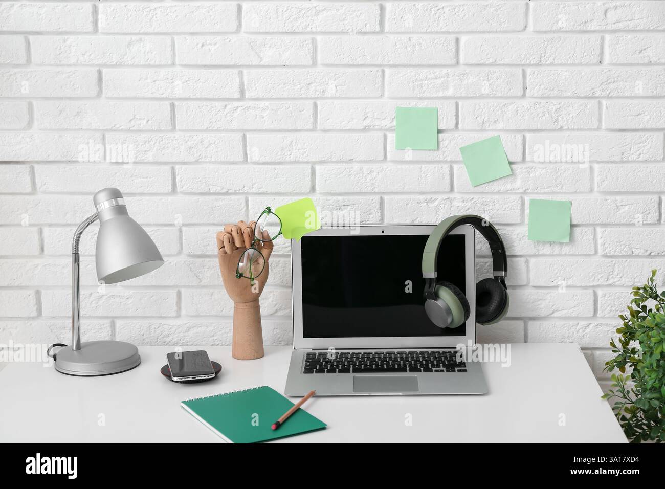 Lieu de travail moderne avec ordinateur portable, lampe, main en bois et papeterie près du mur blanc Banque D'Images