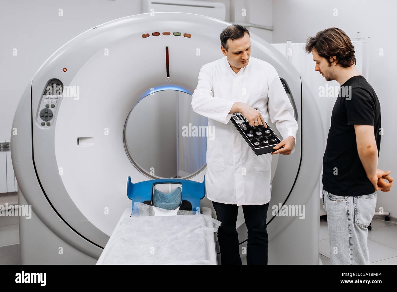 Un médecin dédié effectue un examen IRM tout en s’entretenant avec un patient. Cette image met en valeur le professionnalisme et la compassion dans les soins de santé Banque D'Images