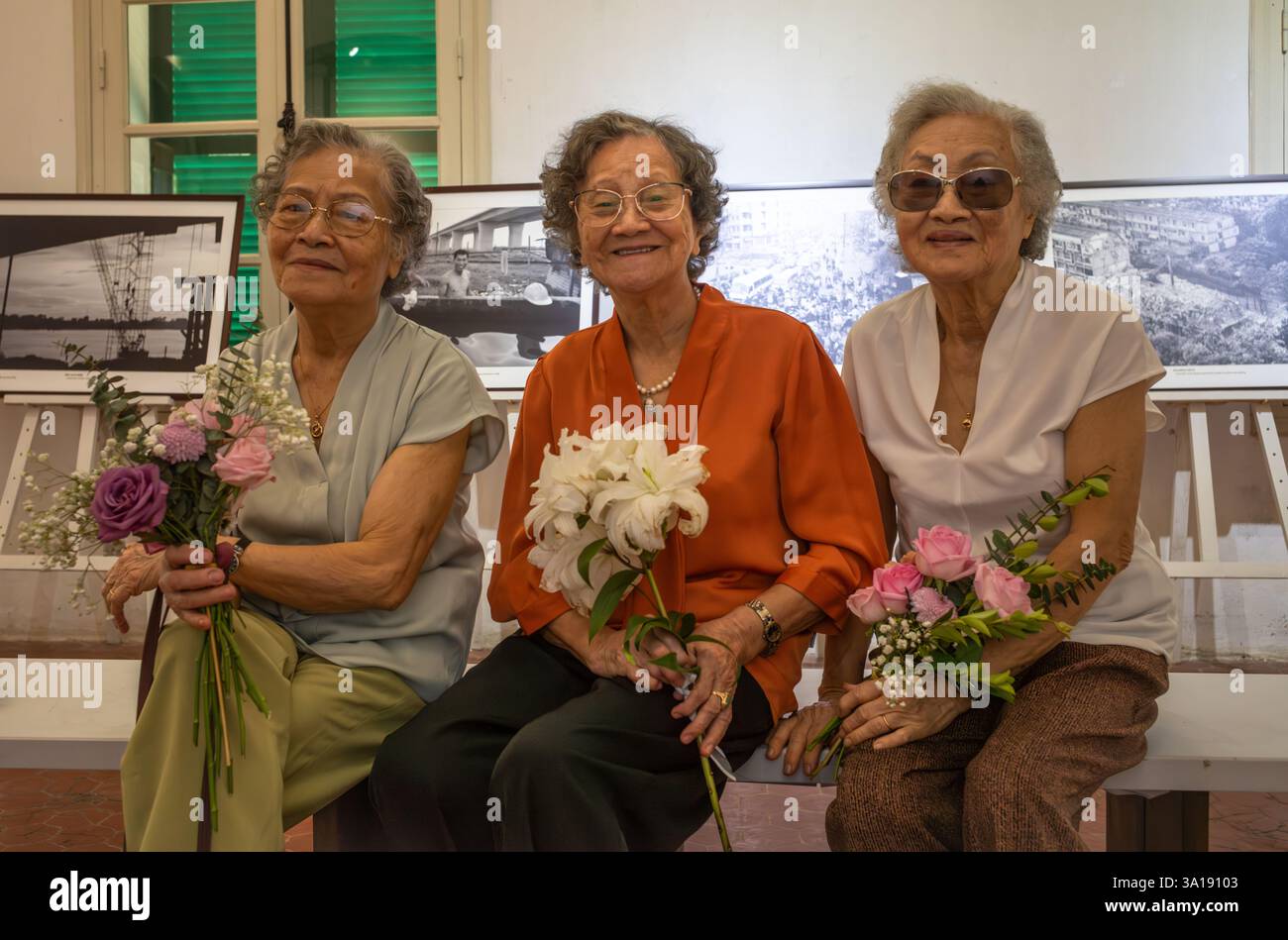 Trois sœurs vietnamiennes âgées tiennent chacune un bouquet de fleurs lors d'une exposition de photographie à Hanoi, au Vietnam Banque D'Images