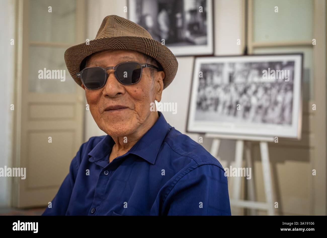 Un vietnamien âgé portant un chapeau Trilby et des lunettes de soleil visite une exposition de photographie à Hanoi, au Vietnam Banque D'Images
