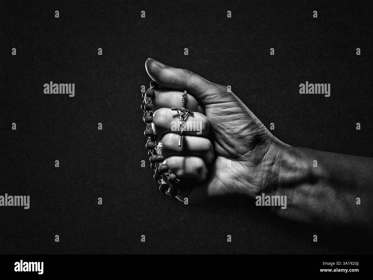 Main avec Rosaire et Croix en noir et blanc sur fond de papier texturé Banque D'Images
