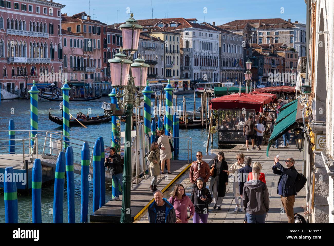 Venise, Italie - 12 octobre 2024 : touristes marchant le long d'une promenade au bord de l'eau près du pont du Rialto avec des bâtiments historiques bordant le Grand canal. Banque D'Images