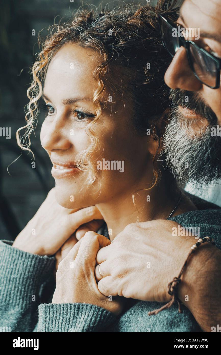 Vue latérale de couple adulte serein se liant et regardant à l'extérieur de la fenêtre à la maison avec l'expression rêveuse. Un homme et une femme embrassant par derrière et prenant la voiture avec amour. Relations heureuses avec les gens Banque D'Images