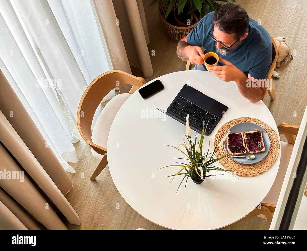 Vue supérieure au deuxième étage de l'homme ayant le temps de petit déjeuner à la maison seul en utilisant un ordinateur portable à la table. Chambre d'hôtel ou concept d'appartement confortable style de vie des gens modernes travaillant tôt boire du café caféine pour commencer Banque D'Images