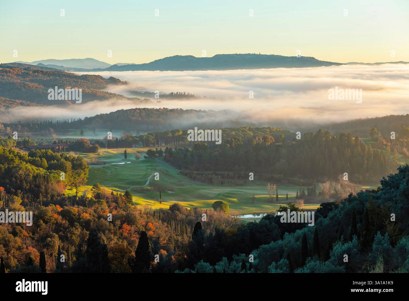 Un brouillard bas enveloppant un parcours de golf pittoresque tandis que des arbres colorés se prélassent de la lueur chaude du lever du soleil à travers la toscane, en italie Banque D'Images