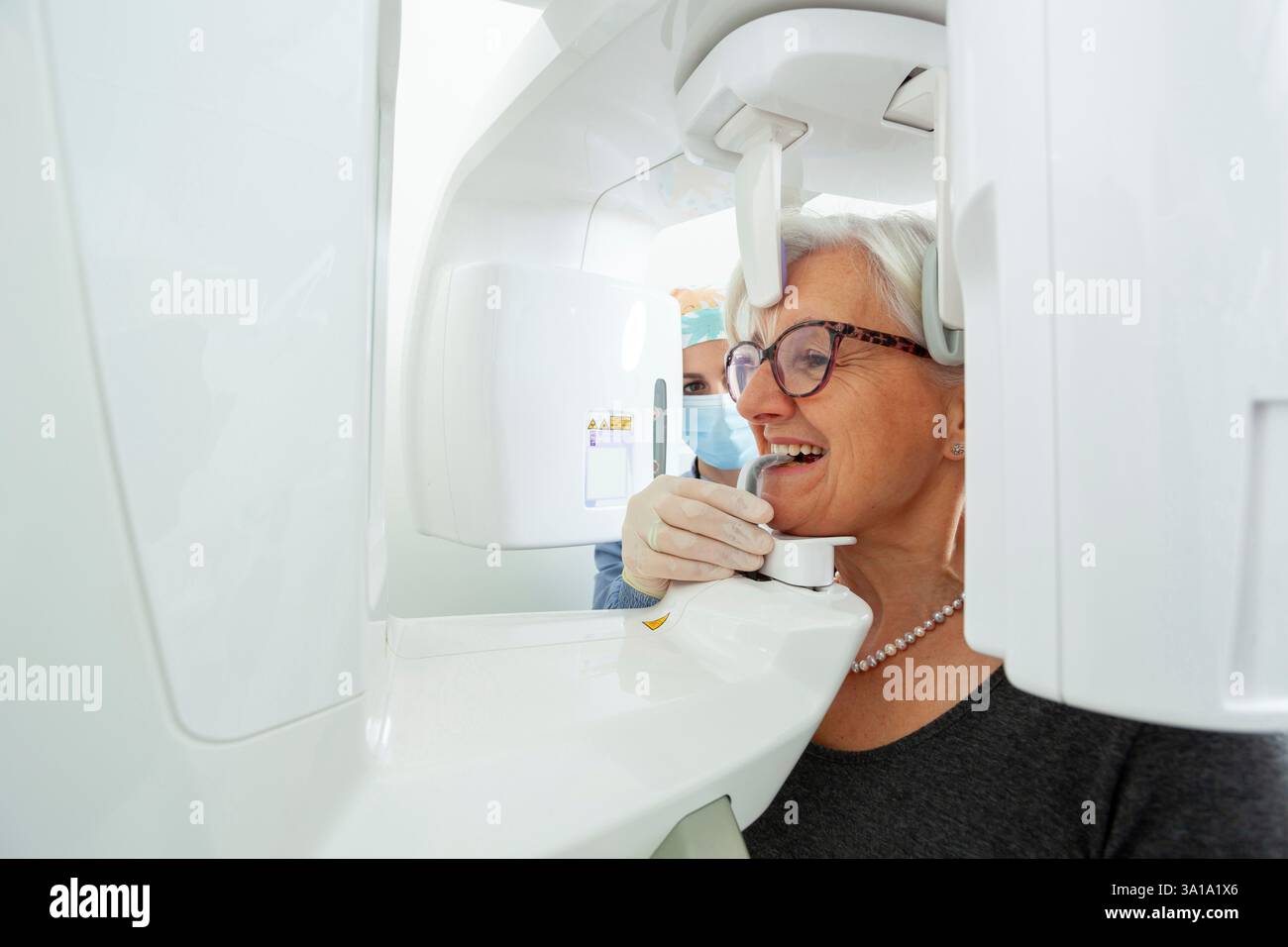 Dentiste ajustant la machine à rayons X panoramique tout en fournissant des soins à une femme âgée dans une clinique dentaire moderne axée sur la santé bucco-dentaire Banque D'Images