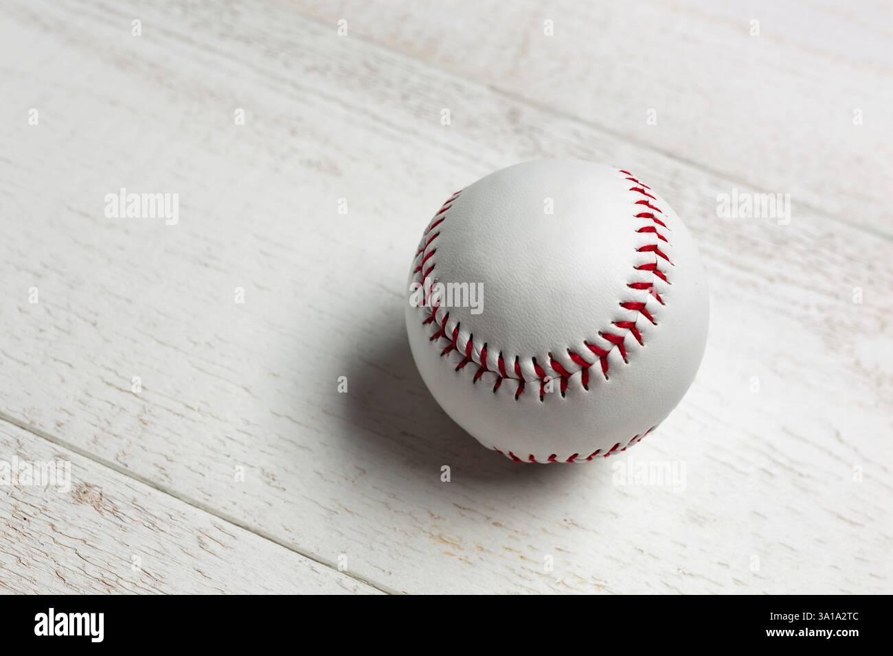 Balle de baseball blanc piqué avec filetage épais rouge en cuir véritable sur un fond de bois blanc. Banque D'Images