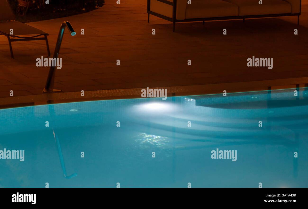 Détendez-vous au bord d'une piscine éclairée la nuit, son eau bleue scintillante sous une lumière douce, créant une oasis de paix parfaite pour se détendre et échapper à l'agitation quotidienne Banque D'Images