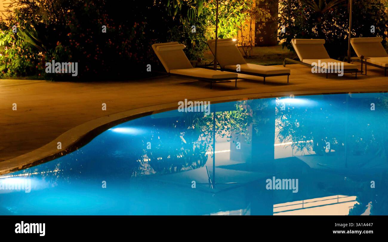 Piscine luxueuse la nuit, magnifiquement éclairée, arbres réfléchissants. L'eau bleue scintille sous les lumières, créant une atmosphère sereine pour la détente. Parfait pour une évasion tropicale Banque D'Images